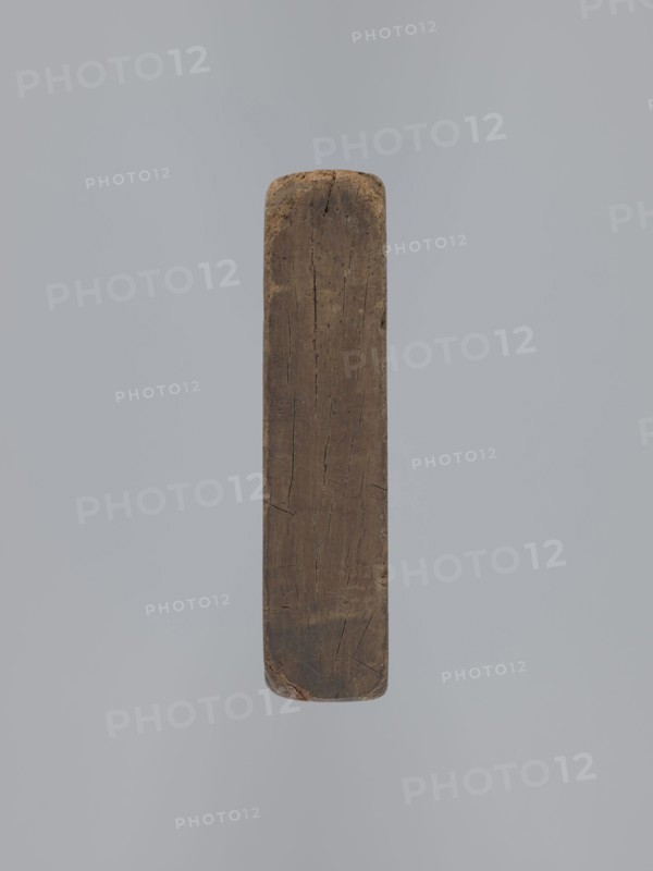 Double-sided gingerbread mould. Obverse: vase with flowers within an oval frame surrounded by a wreath of leaves. Reverse: rectangular recess with a plant ornament, rose motif, and the initials E and G. Rectangular mould, height 16.5 cm, width 11.5 cm, depth 2.7 cm. Gingerbreads, wreaths, applied art, floral decorations, folk motifs. Silesia Province of Silesia, 18th–19th century., A vertical worn wooden beam with a rounded top and bottom floats against a plain light gray background; the wood shows weathered textures with visible cracks and grain, and its colors include brown and darker brown tones with hints of tan and a few darker spots, while the background is light gray.