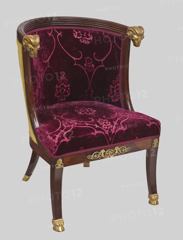 Chair, Empire style mahogany chair with padded seat and backrest, upholstered with patterned velvet upholstery dated early 20th century. Early 19th century. Semicircular seat connected to an arched backrest; fluted upper frame terminating in carved and gilded ram's heads. Arched side panels smoothly connect with side frames. Front legs tilt forward, carved and gilded feet shaped like hooves; rear legs curve diagonally backward, terminating in brass clamps. Brass fittings on the front frame: central volute-shaped plant twig with a palmette and two cornucopias, with palmettes on the ankles. Non-original upholstery: silk velvet with a large net pattern of palmettes and flowers in channel-shaped frames — purple background with light yellow pattern; light yellow fabric on the back of the backrest; fabrics fastened with densely studded brass headers. Materials: mahogany, giltwood, brass, velvet. Height 80.3 cm, width 56.4 cm, depth 60.7 cm. Place of origin: Italy, and France upholstery. Repo...
