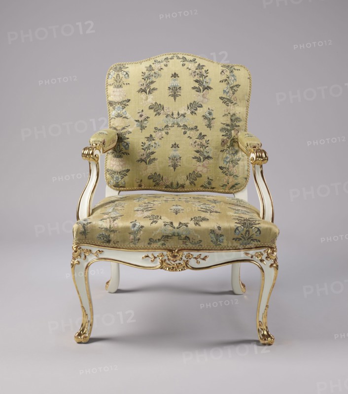 Armchair, Rococo style, floral decoration, cabriole legs, silk fabrics, 18th-century patterned floral fabrics. Upholstered seat, backrest, armrests, carved, white-lacquered and gilded. Cabriole legs, arched into the frame, cut out in a wave-like manner at the bottom; trapezoidal seat with a slightly bulging front frame. Disc-shaped backrest, nearly square, topped with an arch, with slightly concave side rails, straight in line with the sitter's back, slightly tilted with a clearance. Armrests with a volute at the front end, on recessed, slightly S-shaped supports. Edges of all frame elements highlighted with a gilded half-cylinder. Central part of the front frame and upper part of the front legs with carved floral decorations; ends of the armrests and the feet with gilded acanthus leaves. Entire piece reupholstered with cream-colored silk fabric satin-weave background, accented with colored silk and brocaded twill weave with silver thread; decorated with wreaths and alternating vertica...