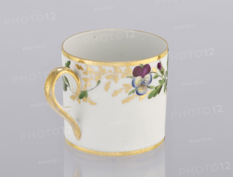 Cup with pansies, Korzec Porcelain and Faience Manufactory, 1790–1832. Cylindrical cup litron, c.1805–1821. Around the upper part of the bowl under the rim: a trail of gilded twigs and colorful pansies; gilded rim. Loop handle, gilded. Porcelain. Place of origin: Korzec, Volhynian Governorate. Vessel. Height 6.1 cm; width 8.8 cm; diameter 6.5 cm., A white ceramic cup with a gold rim at the top and bottom and a gold-painted handle, decorated around the upper exterior with a floral motif in purple, blue, green, and gold leaves against a light gray background.