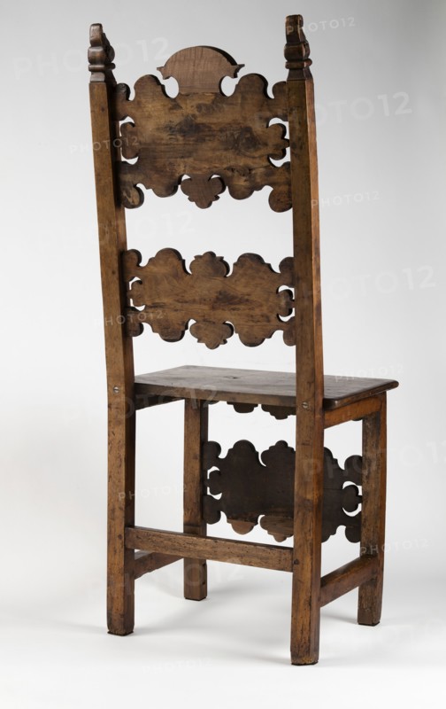 Chair, carved, reclaimed, volutes ornament, Renaissance style. CHAIR with a board seat and a high backrest composed of two boards with a wavy, openwork edge, supported by four straight, angular legs, the rear ones merging into slightly rearward-sloping backrest stiles. Legs fastened with casement binding with angular joints; front legs additionally joined at mid-height by a decorative board shaped analogously to the backrest boards carved with C- and S-shaped acanthus leaves, with single rectangular fields framed with inlaid veining. Side frames angular and narrow; front carved with a lower outline repeating the edge of the backrest boards and front legs. Seat edge profiled as a half-cylinder with a step. Finials of the side backrest frames in the form of a volute. Early 17th century; 4th quarter of the 19th century. Southern Germany ; Lombardy . Piece of furniture, seating piece. Height 121.5 cm; width 51 cm; depth 45.2 cm., A tall wooden chair with a high back featuring decorative cu...