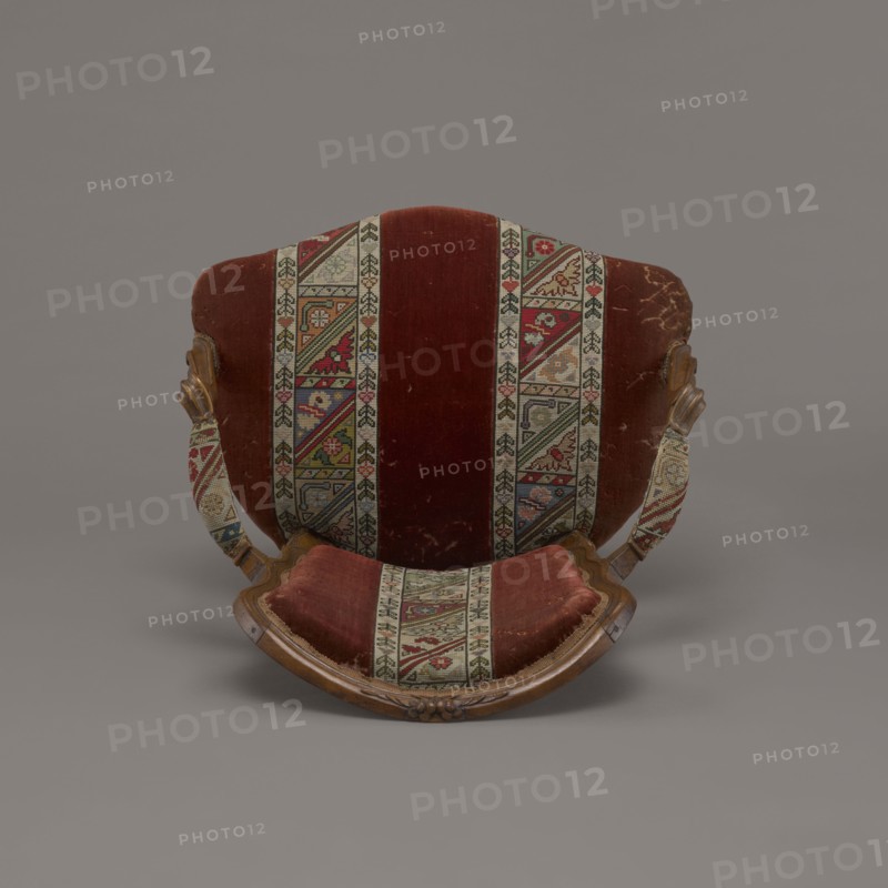 Armchair, rococo, flowers, geometric ornament, ca. 1760, France; piece of furniture seating piece; height 85.5 cm, width 62 cm, depth 60 cm., An upholstered chair viewed from the front showing a curved wooden frame and a fabric back and seat with a striped patterned banding; the visible colors include deep red, beige, green, blue, brown, and hints of yellow and pink, with the wood showing warm brown tones and the background a neutral gray.