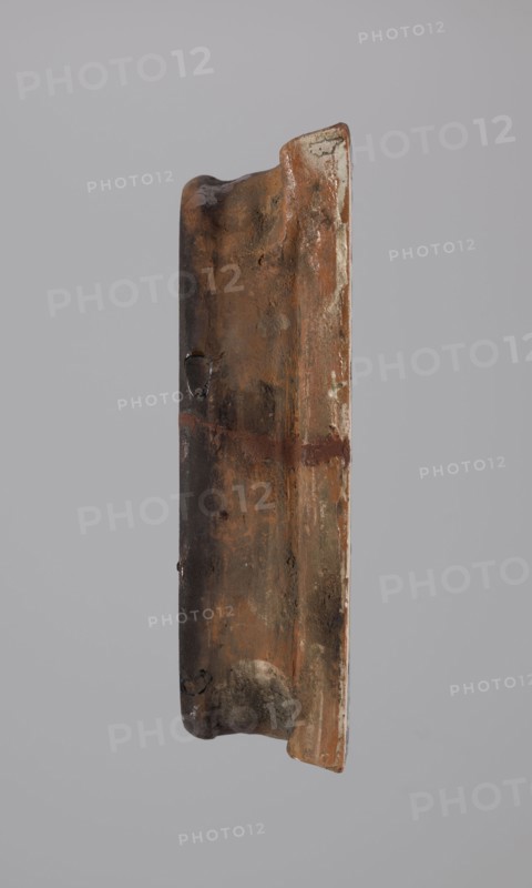 Tile, tiles, Hutsulshchyna, stoves, saints, 1851, with a representation of a saint, Hutsulshchyna, tile, height 23.7 cm, width 20.0 cm, depth 6.0 cm, An upright, elongated object with a rough, weathered surface showing a range of brown and rust tones, including dark brown, reddish-brown, and lighter tan areas, with patches of gray and small areas of off-white along one edge; the object has an irregular, slightly curved profile with worn, rounded ends and a shallow groove running vertically, plus a few darker spots and smudges and subtle shiny patches suggesting a glazed or polished finish against a plain light gray background.