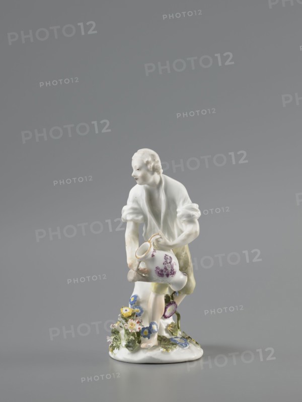 Gardener, Koenigliche Porzellain Fabrique, Meissen 1710–1763; Kaendler, Johann Joachim 1706–1775 sculptor? ; Reinicke, Peter 1715–1768 sculptor? ; gardeners, figurine. On a circular base with a high tree trunk and plastic tufts of flowers stands a slightly bent barefoot man, leaning against the trunk, in knee-length trousers and a luxurious shirt with rolled-up sleeves; he holds a watering can in his left hand, tilting it to water the flowers, and supports the spout with a strainer in the palm of his other hand. Ca. 1760. Meissen, Saxony, Germany. Porcelain figurine; height 12 cm., A small porcelain figurine of a person leaning forward, wearing a white top with rolled sleeves and pale yellow-green shorts, holding a white jug with purple floral decoration, standing on a white base adorned with a group of small colorful flowers in blue, yellow, pink, and green foliage against a neutral gray background.