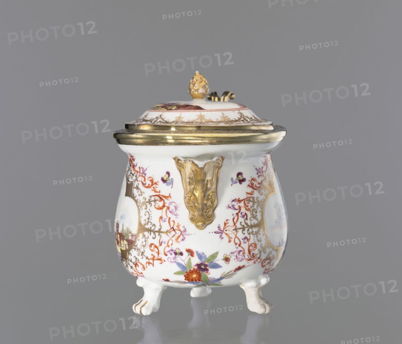 Milk jug, with lid, Augsburg city co-creator, Koenigliche Porzellain Fabrique, Meissen 1710-1763 author, Jug with a squat, spherical, slightly pear-shaped body with a collar around the edge, on three lion-paw legs, with an added triangular, gilded spout with leafy volutes at the base; S-shaped, ribbon-shaped handle, made of leafy, gilded rocaille sections. A slightly arched lid with a pinecone handle, in a gilded silver frame, mounted on a hinge at the rim of the jug. On the belly are two colorful miniatures: 1 a port scene with architecture on a high bank and staffage, 2 city walls over water, with a stone bridge, a boat, and staffage on the bridge. The miniatures are set in 4-leaf gilded lace frames, complemented by a brick-red and purple Regency ornament. Under the spout, beside it, and next to the handle are twigs and projections of Indianische Blumen. On the lid, two port scenes are inscribed in a brick-red circle; a trail of gilded lace surrounds the miniature. Gilded handles, sp...