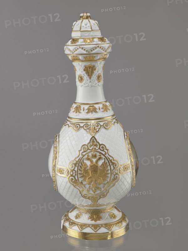 Bottle-shaped vase with a domed lid. Embossed and colorfully painted decoration. Four medallions set against a rococo latticework – a miniature portrait of Tsar Alexander II in ceremonial military uniform with epaulettes and a blue ribbon, the Tsar's monogram, and the Tsar's double-headed eagle on the other two. Gilded floral and plant elements. A gap at the base, worn gilding. Made 1869, St. Petersburg, Russia. Porcelain vessel, height 49.5 cm, width 22 cm. Modeller: August Karlowicz 1817–1904. Manufacturer: Imperial Porcelain Factory in St. Petersburg 1744–1917., A decorative ceramic vessel with an elongated, bulbous body and a tall neck topped by a domed lid sits against a plain gray background; the vessel is primarily white with ornate gold accents and raised decorative patterns, including scrollwork, floral motifs, and a framed heraldic double-headed eagle medallion on the body, a textured lattice pattern on the white surface, gilt bands and leaf-like ornamentation around the neck...