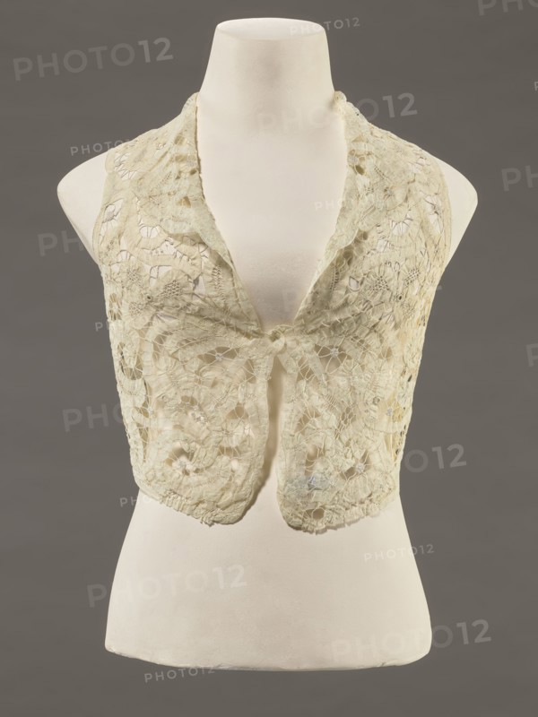 Bodice, lace, provenance, bodice; women's clothing; fashion. Pattern of rosettes connected by large spiders and heads; pattern of stylized floral motifs. 19th century, France. Clothing accessory. Height 36 cm; circumference 63 cm., A garment displayed on a mannequin torso features a sleeveless, open-front design made of delicate lace with floral and circular motifs; the lace appears in pale cream and off-white tones with subtle variations in shading, and the mannequin is an ivory-white color set against a muted gray background.