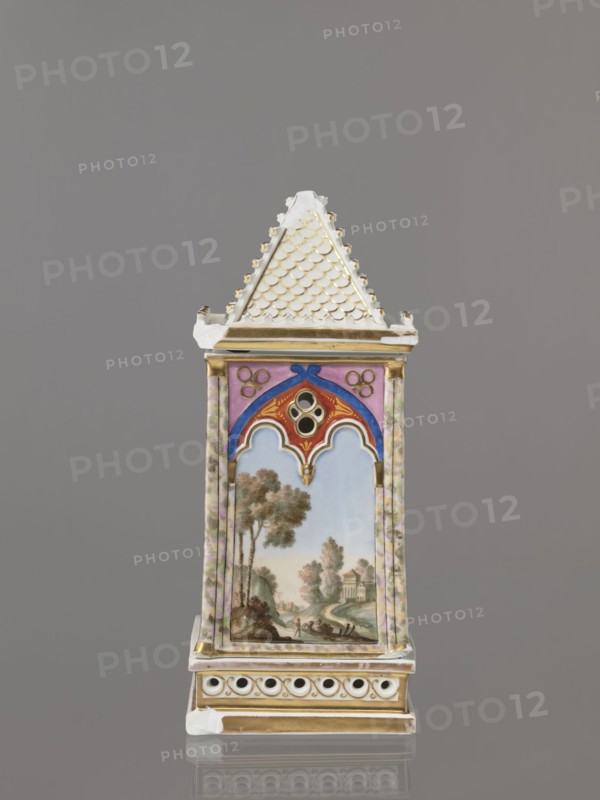 Night lamp by Alexander Popow porcelain manufacturer; 1806–1872. Neo-Gothic porcelain lamp, composed of three parts: base, lamp, and cover. Base has a horizontal row of holes on each side forming a decorative trail. Cube-shaped lamp in neo-Gothic style with arcades shaped like tracery, painted with colorful landscapes: two with motifs of flowering bushes primrose and jasmine, floral motifs against a landscape background, and two landscapes with an architectural motif. 19th century, Gorbunovo, Russia. Height 32.2 cm, width 13 cm., A tall, narrow porcelain object shaped like a small tower with a steep, textured roof in white and gold sits against a gray background; the upper roof section has a scalloped pattern in white highlighted with gold, and gold trim appears below it. The tower's central panel features a painted pastoral scene with a blue sky, green and brown trees, and buildings in muted earth tones, framed by decorative arches in red, blue, pink, and gold; the sides of the panel ...