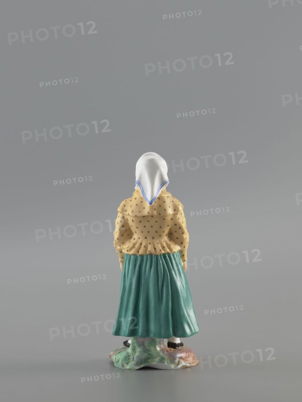 Figurine: Peasant Woman, Popov, Alexander porcelain factory; 1806–1872, figurine depicting a woman in a white scarf with a blue border on her head, wearing a green skirt and apron with red stripes, a yellowish caftan with black dots. Base missing. 1830–1840, Gorbunovo, Russia. Height 3.5 cm; width 6.0 cm; depth 5.7 cm., A small ceramic figurine of a person seen from the back wearing a white head covering with blue trim, a yellow top with a small dark pattern, and a green skirt standing on a multicolored base; the background is a uniform gray.