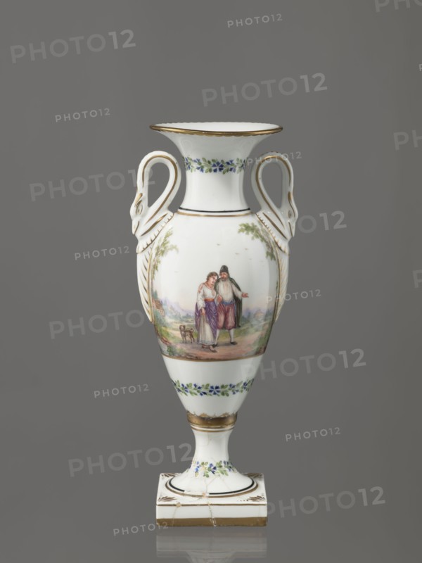Amphora vase, Imperial Porcelain Factory in St. Petersburg 1744–1917. Amphora vase with an ovoid belly, slender neck flaring at the top, high foot on a square plinth. Two handles in the form of swans. Colorfully painted: trails of small flowers on the foot, neck, and lower part of the belly. On the belly, two miniatures depicting genre scenes in a rural landscape: a woman with a pole water carrier siudy, koromyslo and a couple with a dog. Base cracked and glued. Early 19th century, St. Petersburg, Russia. Figurine/vase. Height 26.5 cm, width 11.0 cm, depth 9.0 cm., A white porcelain vase with a flared rim and a pedestal base, decorated with gold trim and bands of small blue and green floral motifs, featuring a painted pastoral scene of a couple standing together on the body with a small animal nearby, and ornate curved handles shaped like stylized swans attached to the shoulders; colors visible include white, gold, blue, green, brown, purple, and muted flesh tones, set against a neutra...