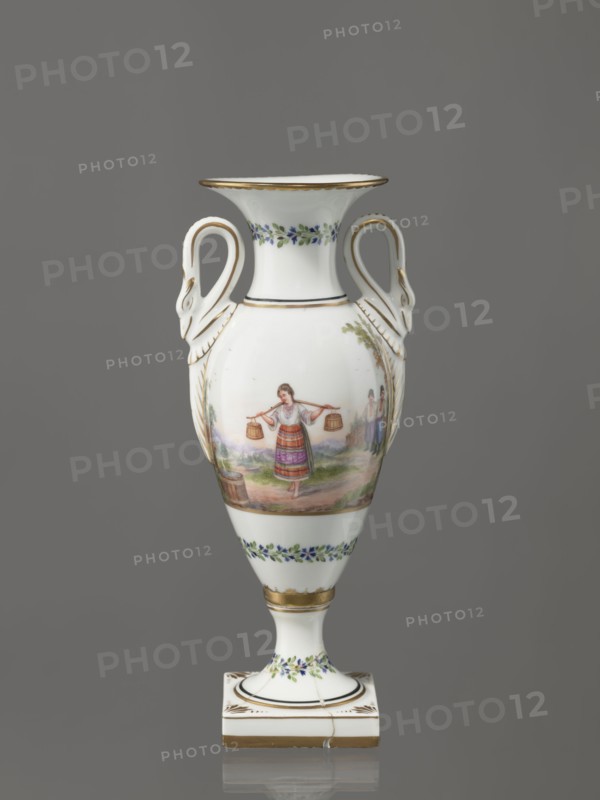 Amphora vase, Imperial Porcelain Factory in St. Petersburg 1744–1917. Genre miniatures, genre scenes in landscapes, amphoras, plant decoration, water carriers, water. Amphora vase with an ovoid belly. Slender neck, flaring at the top, high foot on a square plinth. Two handles in the form of swans. Colorfully painted: trails of small flowers on the foot, neck, and lower part of the belly. On the belly, two miniatures depicting genre scenes in a rural landscape: a woman with a pole water carrier siudy, koromyslo and a couple with a dog. Base cracked and glued. Early 19th century, Russia, St. Petersburg. Figurine, vase. Height 26.5 cm, width 11.0 cm, depth 9.0 cm., A white porcelain urn with a glossy finish stands against a plain gray background, featuring a flared rim and a pedestal foot on a square base; the urn has curved handles shaped like stylized swan heads and is decorated with painted scenes and floral garlands. The central painted scene shows a person wearing a multicolored dres...