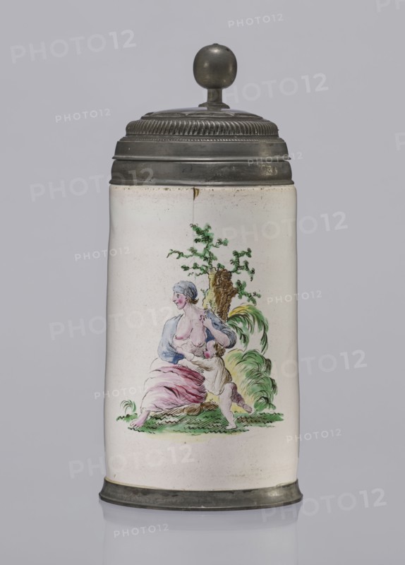 Cylindrical tankard in a pewter frame, Prószków Slaski faience factory; 1763–1853. White, painted in colors. From the front, a depiction of a barefoot woman sitting under a tree, her blouse unbuttoned, revealing her breasts. The woman, head turned to the right, supports with her right hand a small child, dressed in a short T-shirt, running towards her from the left. It can be interpreted as an allegorical representation of Maternitas motherhood. The representation is painted with some freedom. Late 18th century, Silesia Province of Silesia. Vessel; height 24.0 cm, width 15.0 cm, depth 10.5 cm., A tall cylindrical ceramic tankard with a rounded metal lid and finial, the lid and base are a dark metallic gray and the ceramic body is an off-white or cream color; on the front of the body is a painted scene showing a seated woman with pale skin and light bluish-gray hair wearing a blue top and a pink skirt, a small child with pale skin and light-colored hair reaches up toward her while leani...