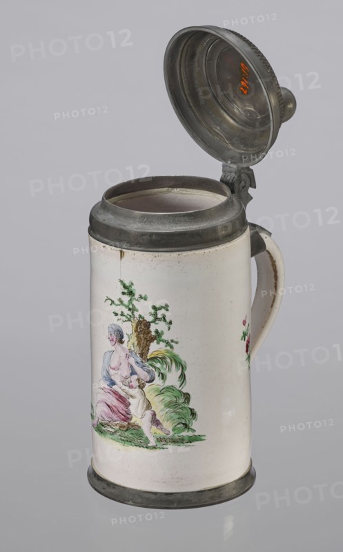 Cylindrical tankard in a pewter frame, Prószków Slaski faience factory; 1763–1853. White, painted in colors. From the front, a depiction of a barefoot woman sitting under a tree, her blouse unbuttoned revealing her breasts. The woman, head turned to the right, supports with her right hand a small child, dressed in a short T-shirt, running towards her from the left. It can be interpreted as an allegorical representation of Maternitas motherhood. The representation is painted with some freedom. Late 18th century, Silesia Province of Silesia. Vessel; height 24.0 cm, width 15.0 cm, depth 10.5 cm., A ceramic tankard with a hinged metal lid is shown against a pale gray background; the tankard is mostly white with metal rim and base in a dull gray, and a matching metal lid that is open, showing the interior metallic surface. The body features a painted scene in soft colors including green, pink, blue, yellow, and flesh tones depicting a seated woman and a child by a tree with foliage and gras...
