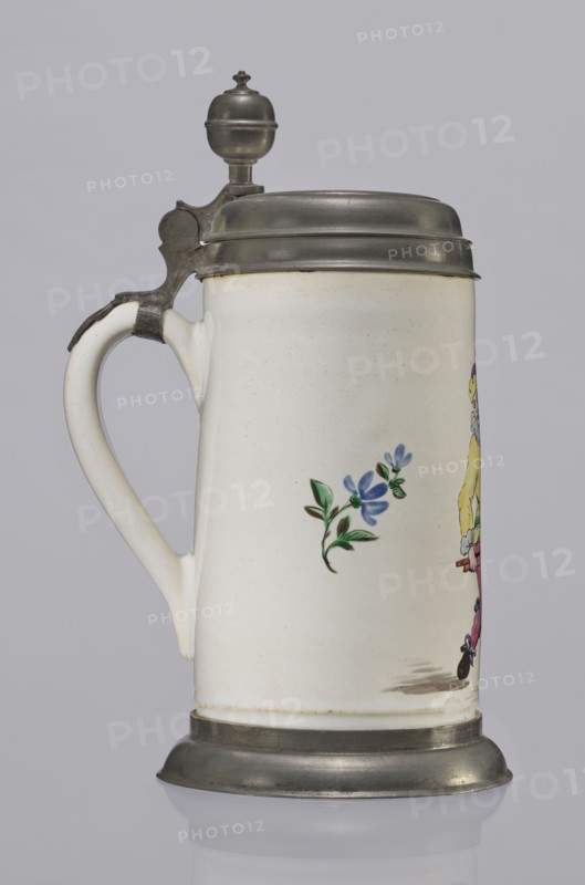 Tin-mounted tankard, Prószków Slaski faience factory 1763–1853. White cylindrical tankard with a pewter mount. On the front is a depiction of an obese musician playing a double bass, shown in vigorous movement; the musician wears a yellow jacket, purple pantaloons, and a lilac hat with a yellow brim. Floral sprigs on the sides. Tin cover engraved CGH/1811. Late 18th century. Silesia Province of Silesia, 1742–1918. Vessel. Height 24.0 cm; width 15.0 cm; depth 9.5 cm., A ceramic stein with a white body and a curved handle, topped with a metal hinged lid and finial and with a metal base, showing a small painted blue flower with green leaves on its side and part of a colorful figurative decoration at the edge; visible colors include white, gray, blue, green, yellow, pink, black, and metallic gray.