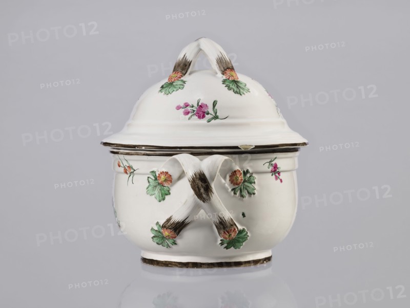 Vase with lid, Prószków Slaski faience factory; 1763–1853, floral decorations, soup tureen, roses, provenance repossession. Egg-shaped soup tureen with a lid in the form of a flattened ellipsoid/hemisphere. Handles of the vase and lid are two crossed ribbons. Decorated with small painted floral sprigs and large bouquets of multicolored flowers; on both sides of the vase and lid are bouquets with a pink rose. Handles adorned with vermilion daisies with large green leaves. Rim of vase and cover painted brown. Circa 1785. Province of Silesia 1742–1918, Silesia, Prószków Slaski. Vessel; height 25.5 cm, length 35.5 cm., A white ceramic lidded vessel with a rounded body and a domed lid topped by a looped handle, decorated with painted floral motifs in green, pink, and orange, and accented with brown brushstrokes on the handles and rim; the piece rests on a short base and sits against a pale gray background.