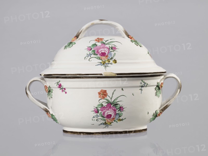 Vase with lid, Prószków Slaski faience factory ca. 1785, 1763–1853. Egg-shaped soup tureen with lid in the form of a flattened ellipsoid/hemisphere. Handles of the vase and lid are two crossed ribbons. Decorated with small painted floral sprigs and large bouquets of multicolored flowers; on both sides of the vase and lid are bouquets with a pink rose. Handles are adorned with vermilion daisies with large green leaves. Rim of vase and cover painted brown. Province of Silesia Silesia, Prószków Slaski. Vessel; height 25.5 cm, length 35.5 cm., A white ceramic lidded tureen with a curved handle on the lid and two looped side handles, decorated with painted floral motifs including pink and purple roses, orange and yellow flowers, and green leaves; the rim and handles show brownish accents and wear, and the piece sits on a shallow base against a pale gray background.