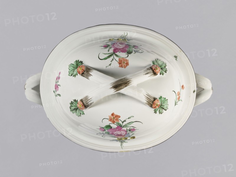 Vase with lid, Prószków Slaski faience factory; 1763–1853. Egg-shaped soup tureen with a lid in the form of a flattened ellipsoid/hemisphere. Handles of vase and lid formed as two crossed ribbons. Decorated with small painted floral projections and large bouquets of multicolored flowers; on both sides of vase and lid are bouquets with a pink rose. Handles adorned with vermilion daisies with large green leaves. Rim of vase and cover painted brown. Ca. 1785. Province of Silesia 1742–1918; Silesia, Prószków Slaski. Vessel. Height 25.5 cm; length 35.5 cm., A white ceramic dish with a lid and handles is shown from above, featuring a crossed pair of raised ribs on the lid; the surface has painted floral decorations in green, pink, orange, and yellow with touches of pale blue and brown brush marks on the ribs, and the background is a pale gray.