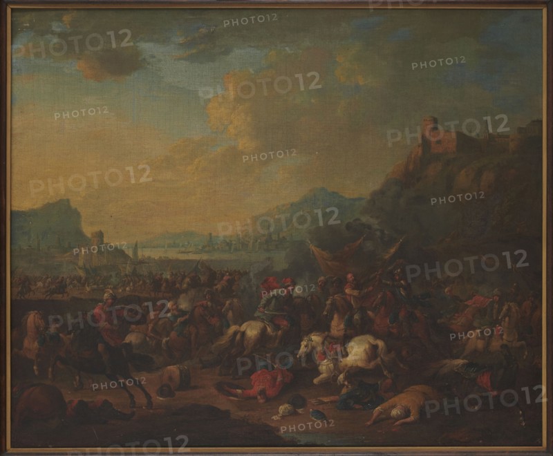 Skirmish against the backdrop of a mountainous landscape; Rubens, Arnold Frans 1687–1719, painter; painting depicting battle scenes and landscapes; Flemish painting; 17th/18th century; oil on panel height 49 cm, width 59 cm; restitution, A large painted scene shows a dramatic outdoor landscape with a broad sky of muted blues, dusty yellows, and grayish clouds. In the foreground a chaotic battle scene is visible with many mounted figures and fallen figures on the ground; horses appear in colors including brown, black, and white. Several figures wear garments in red, green, and blue tones, and some wear head coverings in pale and dark shades. There are a few banners or cloths in warm colors held above the combatants and some smoke or dark haze rising near the center-right. The middle ground contains a busy shoreline or plain with a group of small structures and silhouettes of distant buildings along a waterline, rendered in soft blues and grays. To the right a rocky hillside rises to a f...