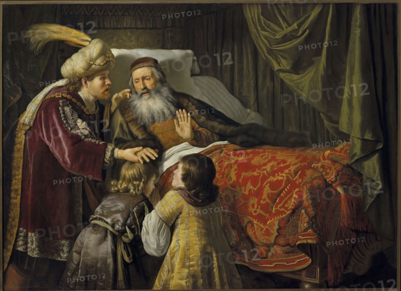 Jacob Blessing the Sons of Joseph, Victors, Jan 1619–1676, painter; oil painting, 1650s; biblical scene depicting Jacob the Patriarch blessing Ephraim and Manasseh Joseph; height 136 cm, width 190 cm; subject inscriptions: Jacob, Ephraim, Manasseh., An interior scene shows an older man with a long gray beard reclining on a bed with a white pillow and a richly patterned red and gold coverlet, a dark fur-lined cloak over his shoulders and a brown cap on his head; he raises a hand while looking toward a younger man standing beside the bed who wears a large cream turban with a yellow plume and a deep burgundy robe trimmed with ornate metallic embroidery. Two children stand at the bedside facing the older man; one child has light blond hair and a brown garment with a tied sash, and the other has darker hair and a gold-striped dress with white sleeves. Behind and around the bed are heavy draperies in shades of dark green and olive, and the overall palette includes reds, golds, browns, burgun...