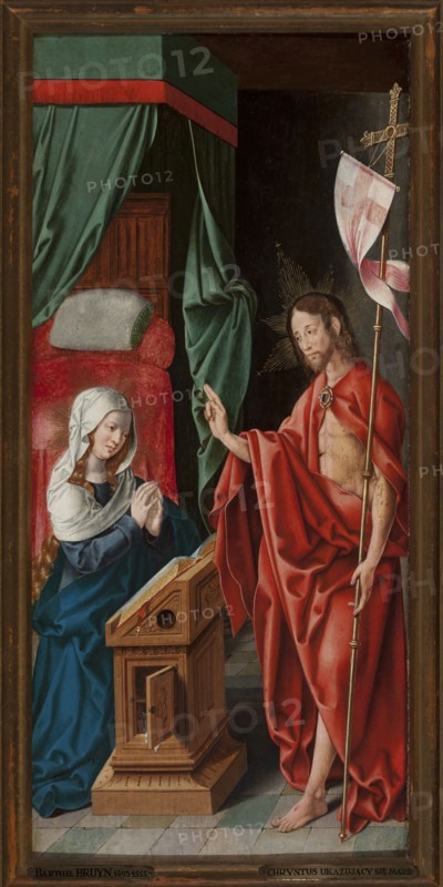 Christ Appearing to Mary, Bartholomäus Bruyn 1493–c.1555, German painting, religious/biblical scene depicting Mary mother of Jesus and the Resurrected Christ, interiors, crosses attribute. Painted c.1515–1525. Painting with frame: height 71 cm, width 35 cm., A vertical painted scene framed by a wooden border shows an interior with a tiled floor in shades of green and gray, a large draped canopy in green with a red border, and a bed with red upholstery and a pale pillow. On the left, a kneeling woman with pale skin and long blond hair peeking from under a white head covering wears a deep blue robe and has her hands clasped in front of a wooden lectern with carved panels and an open book. On the right, a standing man with pale skin, shoulder-length brown hair, and a short beard is draped in a flowing red cloth that reveals part of his torso; he holds a tall staff topped with a cross-like element adorned with a pink and white banner, and he makes a raised gesture with his other hand. Both...