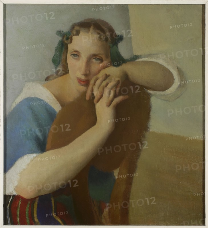 Portrait of a Wife, Jacek Mierzejewski 1883–1925, painter; 1919; interwar period, Poland. Contemporary painting in the Formist style Formists, 1917–1922. Subject: artist's wife; women's portrait. Painting; height 56.5 cm, width 51 cm., A painted portrait of a young woman leaning on the back of a wooden chair, with a pale face, pink lips, and light brown hair tied with green ribbons; she wears a blue garment with white trim and her exposed arms are pale; the chair back is brown and occupies the center foreground; the background shows muted beige and light gray tones and a floor area in warm tan; a few brightly colored striped cloths with red, green, blue, and yellow appear near the lower edge.