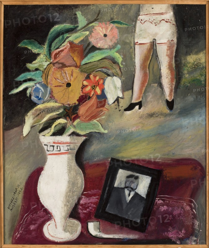 Anniversary of death, Brzeski, Janusz Maria 1907-1957 painter, still lifes, interwar period, contemporary painting, flowers in vases, pictures within pictures, underwear, 1932, Poland, painting, height 55 cm, width 46.2 cm, A painted scene shows a large white vase with decorative trim holding a lush bouquet of flowers and leaves in shades of green, yellow, orange, pink, red, blue, and white, set against a dark and muted background with areas of gray and black. To the right, the lower half of a figure is visible wearing light-colored garments with decorative red trim and black shoes, standing against a textured backdrop with green and brown tones. In the lower area, a deep red surface supports a framed portrait with a dark frame and a monochrome depiction inside, alongside a curved white object, all resting on a mottled red and pink cloth. The overall palette includes white, green, yellow, orange, pink, red, blue, black, gray, and brown.