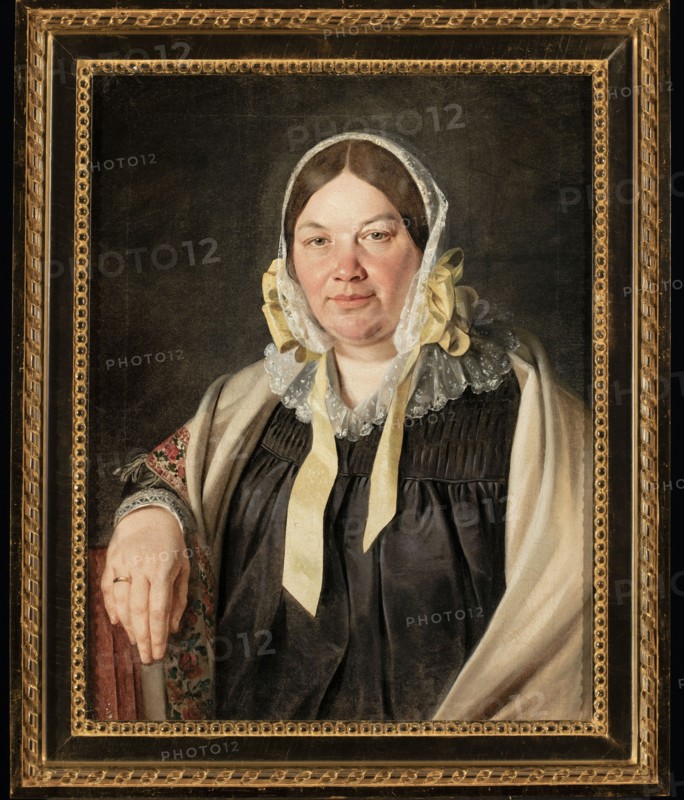 Portrait of Aleksandra Bebnowska, née Cybulska, the painter's mother-in-law; Jan Chrucki 1810–1885, painter; ca. 1845; oil painting; female half-length seated portrait, full-face; Biedermeier style; depiction includes scarf, bonnet, wedding ring., A painted portrait of a seated woman wearing a white lace bonnet with yellow ribbons, a dark dress, and a light shawl draped over one shoulder, her hand resting on a patterned armrest; her face is fair with brown hair, and the background is dark, all set inside an ornate gold frame showing tones of gold and black.