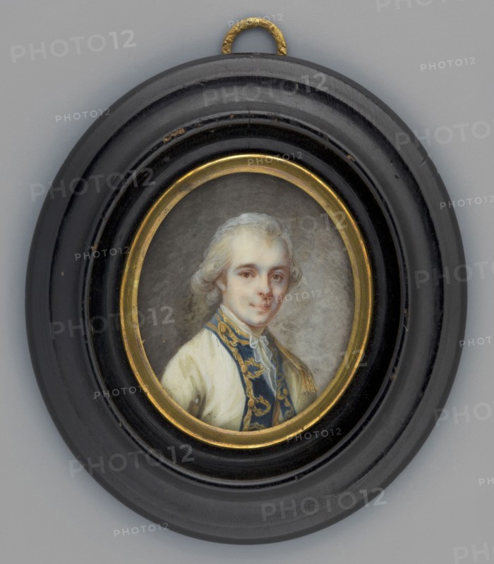Portrait of a young man in a cream tailcoat from the family of the Duke de Cosse-Brissac ?Hyacinthe Hugues Timoleon, unknown artist; aristocracy, male three-quarter portrait; Polish miniature. Bust three-quarter right. White wig tied with a bow at the back of the head; white ears and cravat; cream tailcoat with navy blue lapels embroidered with gold. Background uneven brown-grey, brightened on the right. Oval gilded bronze border; in an oval wooden frame, recessed and profiled, polished to look like mahogany. 1790, France. Miniature; height 4.5 cm, width 3.7 cm., A small oval portrait set in a round black frame with a gold inner rim and a small textured gold hanging loop at the top shows a light-skinned person with powdered white hair styled back, wearing a cream-colored garment and a dark blue garment with gold embroidered trim; the background behind the figure is a muted gray.