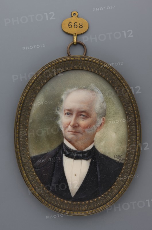 Portrait of an Elderly Man with Sideburns, by Jahn, Friedrich August fl. 1810–1894, painter. Miniature portrait 1894, Germany, bust: almost straight ahead, head three-quarters to the left. Subject: elderly man with gray hair and sideburns, gray eyes; wearing a white shirt, black tie, waistcoat, and frock coat. Hairstyle slicked back. Background: olive clouds/sky. Style: modernism. Materials/format: miniature, height 8.3 cm, width 6.3 cm. Frame: patinated brass with narrow rim and acanthus motif. Provenance note: repossession Jelenia Góra., An oval portrait in an ornate metal frame shows the bust of an older man with light gray hair and sideburns, fair skin with a slightly rosy complexion, and a composed expression; he wears a dark suit jacket and a white shirt with a black bow tie. The frame is a mottled brass or bronze color with decorative raised patterns and a small hanging loop at the top attached to a small oval tag; the background behind the figure is a muted greenish-gray. The v...