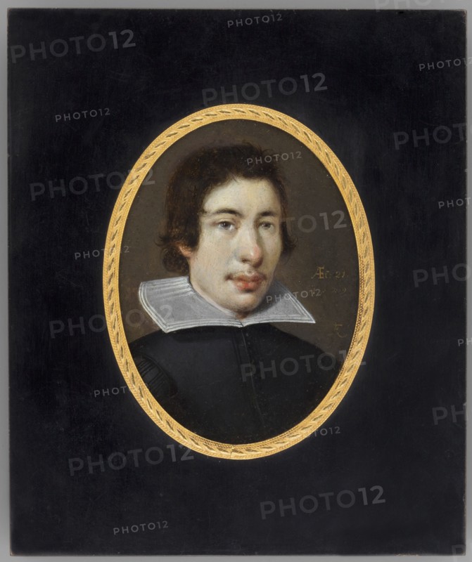 Portrait of a Young Man. Franz Kessler fl. 1580–1650, 1629. Miniature, height 9.8 cm, width 7.1 cm. Bust, 3/4 right. Hair c. brown, eyes grey. Dark olive caftan with white turndown collar; background olive green. Bronze rim binding with polished wood and braided motif on a narrow medallion rim. Inscription on front right: AEf: 21. | 1629 | FK. Reverse inscription noting Franz Kessler, activity 1613–1629 and birthplace Oppenheim. Genre: male portrait; style: miniature/self-portrait., An oval portrait of a young person with medium-length dark brown hair set against a dark background within a decorative gold oval frame; the person has a pale skin tone, visible facial features including dark eyes and slightly parted lips, and wears a black garment with a white, flat, wide collar; colors visible include black, gold, white, pale skin tones, brown, and subtle gray.