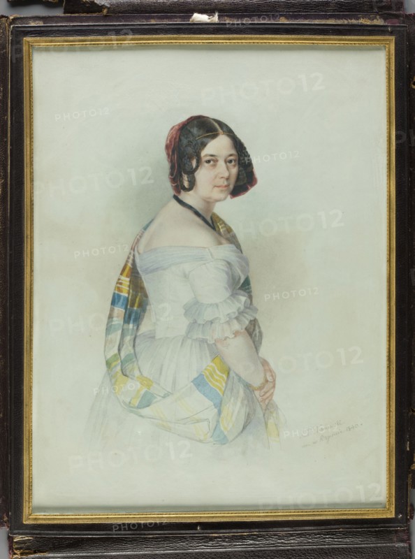 Portrait of Aleksandra, née Stecka, Princess Michal Radziwill. Painter: Jan Ksawery Kaniewski 1805–1867. Miniature, 1840. Standing figure shown from the right side, knee-deep, head three-quarters to the right. Dark brown hair parted in the middle; thin circular braids at the sides; decoration of rusty-red velvet ribbons at the back of the head; a gold chain with a la ferroniere medallion above the forehead; black velvet ribbon at the neck. White dress with a tyftic shawl with yellow and turquoise stripes on the left shoulder; arms lowered and folded. Background slightly watered. Rectangular narrow bronze frame decorated with a palmette, fluting and pearls; in a lockable case of dark purple leather. Inscription: IX Kaniewski/m. in Rome 1840. Dimensions: height 29.2 cm, width 22.3 cm. Subject: Aleksandra Radziwill, née Stecka 1796–1864, wife of Michal IX Radziwill 1778–1850., A framed portrait of a woman shown from the waist up turned slightly to the side, wearing a white off-the-shoulde...