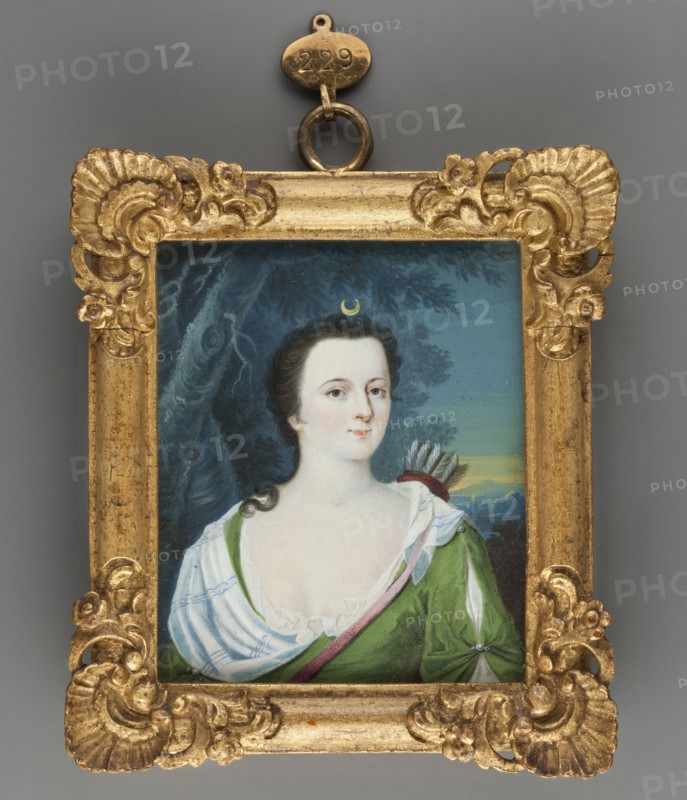 Caroline Louise of Hessen-Darmstadt as Diana 1723–1783, Margravine of Baden; unknown painter; miniature portrait, ca. 1750; watercolour on ivory height 7.8 cm, width 6.5 cm. Inscription/labels: No. 5 | Caroline Luize | Gemahlin des Markgrafen | Carl Friedrich von Baden | Tochter Ludwigs, born 11 July 1723 + 8 April 1783. Called by her contemporaries the Hessian Minerva hessische Minerva. Subjects/themes: antiquity, women, portraits, costumes, female portraits, rulers, amateurs. Repossession provenance: Jelenia Góra., A small rectangular painted portrait set in an ornate gold frame with carved shell and floral motifs around the corners and edges, the frame suspended by a metal loop at the top; the painting shows a fair-skinned woman with dark curled hair and a small crescent-shaped ornament above her forehead, wearing a low white chemise with ruffled trim and a green garment with a diagonal pink sash, a quiver with visible feathers resting behind her shoulder, and a background of dark t...
