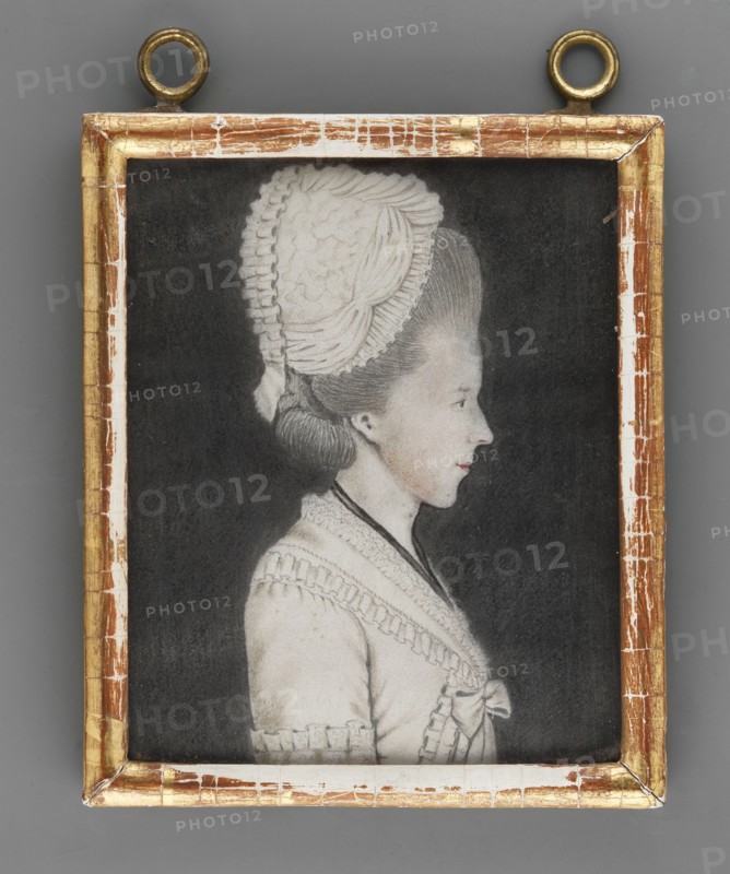 Amalia Eleonora von Solms-Braunfels 1734–1811, princess of Anhalt-Bernburg-Schaumburg; miniature portrait, ca. 1800, Germany. Waist-length right-profile portrait: fair hair covered with a white bonnet, blue eye; black ribbon around the neck, white dress; black background. Frame: wood. On the back of the mounting an inscription: Amalie Eleonore/Furstin zu Anhalt-Bernburg=Schaumburg Tochter/Der Fursten Friederic/Wilhelm zu Solms=Braunfels and two labels one with a fragment of a seal. A card with the inscription: Amalie Eleonore./ Furstin zu Anhalt-Bernburg=/Schaumburg/Geboren Prinzesin von Solms-/Braunfels/Geboren den 22 ten November 1734./ Gestorben den.1810. Miniature, height 11.4 cm, width 9.3 cm. Creator unknown amateur. Subjects: women, rulers; styles: portraits, profiles, female portrait, foreign miniatures., A framed portrait of a woman shown in profile against a dark background, the woman wearing a light-colored dress with decorative trim and a bow at the front, and a tall, textu...