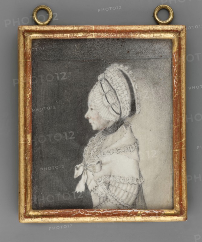 Caroline Katherina von Birkenfeld 1699–1785, third wife of Friedrich Wilhelm I zu Solms-Braunfels. Unknown artist. Ca. 1800. Miniature portrait, profile of a woman in headgear and costume; height 11.7 cm, width 9.1 cm., A framed portrait of a person in profile facing left, depicted in pale tones against a darker background; the person wears a white, lace-trimmed bonnet with decorative bands and a dark ribbon tied under the chin, and a light-colored shawl or dress with lace edging and a bow at the front; the drawing is mostly in shades of gray, black, white, and pale skin tones, and the rectangular frame is gilded with worn gold and reddish-brown areas with visible cracks and two circular hanging rings at the top.
