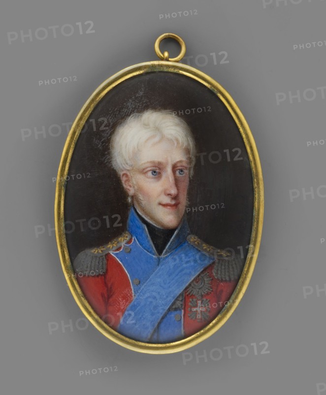 Frederick VI of Denmark 1768–1839, King of Denmark; painted by Johann Gorbitz 1782–1853. Miniature portrait 1815, height 5.3 cm, width 3.7 cm. Bust in full view, head facing right. Depicts a man in a red uniform with blue collar and rebates; wearing the star and ribbon of the Order of the Elephant and the cross of the Order of the Dannebrog. Background plain, brownish. Binding: gilded bronze. Attributions: Anna Chamiec; scientific cards Iza Wiercinska., An oval pendant with a gold frame contains a painted portrait of a young person with pale blond hair and light skin, shown from the chest up against a dark background; they wear a red coat with gray epaulets and decorative gold details, a bright blue sash across the chest, and a black high collar, and the pendant hangs from a small gold loop.