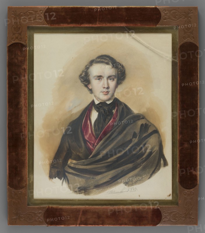 Alfred Józef Potocki 1822–1869, son of Alfred Wojciech and Józefa née Czartoryska, 2nd Entailer of Lancut. Painter: Jan Nepomucen Glowacki 1802–1847. Half-length portrait, head almost straight. Short hair, white shirt and collar, black cravat, burgundy waistcoat, dark brown frock coat and cloak-cape à la Byron. Background: light ocher with a light blue spot. Binding: gilded bronze, velvet, embossed leather. Date: 1843. Place of origin: Poland. Miniature; height 25.2 cm, width 20.8 cm., A framed portrait of a young man shown from the waist up, with wavy dark brown hair and a pale complexion, wearing dark clothing including a black bow at the neck and a draped dark cloak with a deep red inner lining; the background behind him is a soft beige wash. The portrait is set within a narrow gold-colored inner frame and a wider outer frame covered in brown velvet and embossed brown leather at the corners. The visible colors include brown, beige, black, dark red, gold, and pale skin tones.
