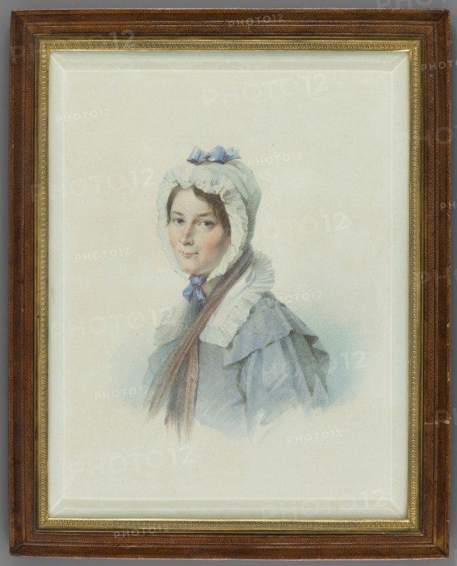 Portrait of Ludwika Hilbertz Soubirau, beloved nurse of Aleksandra Potocka, daughter of Stanislaw Septym and Katarzyna née Branicka; after Thomas Lawrence 1769–1830 by an unknown painter; miniature, 1840, Rome; height 24.0 cm, width 18.5 cm; costumes, women, female portrait, headgear., A framed watercolor portrait of a woman wearing a bonnet and cloak, with a pale face and dark hair peeking from beneath the bonnet; the bonnet is light with a small bow on top and ruffled trim, and a ribbon tied under her chin. The cloak and dress are in soft blue-gray tones with layered collars and ruffled details, and a long brown scarf or hair strand drapes down over the front. The background is a pale, off-white wash, and the portrait is set within a gold inner frame and a wider brown outer frame showing wood grain. Colors visible include white, cream, pale blue, blue-gray, brown, gold, and flesh tones.
