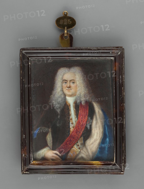 Frederick William I of Prussia? 1688–1740, unknown artist, amateur painter. Portrait, waist-length, left; men's portrait waist-length, left. Subject: middle-aged man wearing a long white wig with curls parted in the middle; sapphire coat lined with white fur, white embroidered vest, white shirt; silver star of an order on a red ribbon. Style: foreign miniature, half-length, almost straight pose. Background: brown. Inscription/marks: orders. Provenance note: repossession Jelenia Góra. Object: miniature, tortoiseshell binding rim profiled, narrow, dated circa 1770. Dimensions: height 7.8 cm, width 6.3 cm., A framed portrait of a person with pale skin and a large powdered wig, wearing dark clothing with a red sash draped across the chest and a light-colored fur or fabric over one shoulder; the figure's hands are visible at the lower edge of the portrait. The rectangular frame is dark brown with some worn areas and small scratches, and a metallic hanger with a small oval plate is attached ...