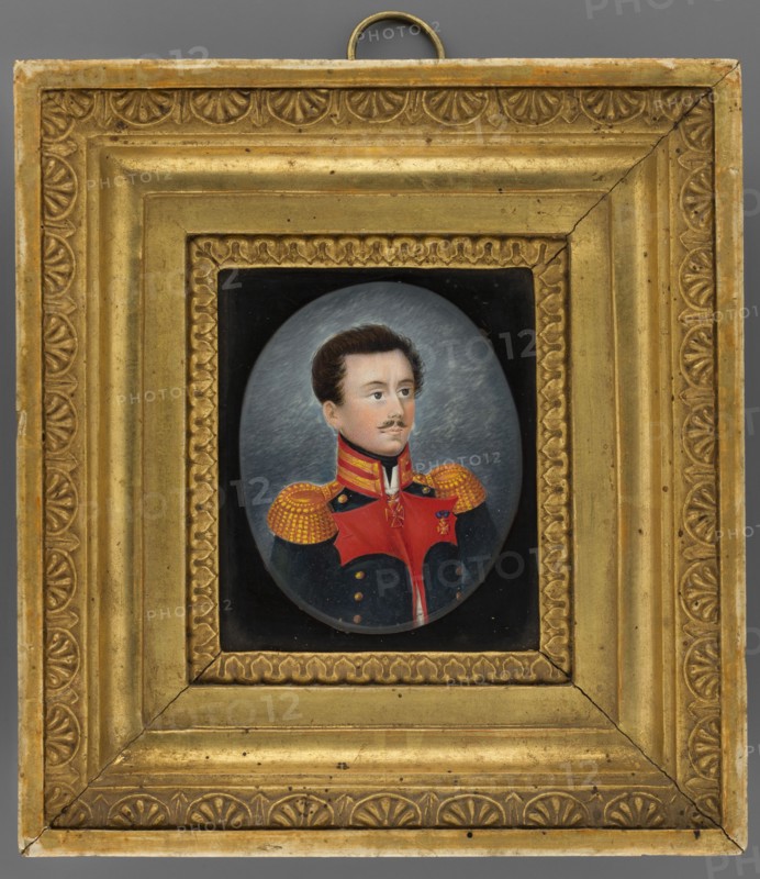 Portrait of a colonel of the Russian army, unknown painter, miniature, height 7.3 cm, width 5.8 cm; uniforms; orders: Order of St. Vladimir 3rd class, Polish Badge of Honour; 1830; male portrait of a soldier., A framed oval portrait of a man in a military uniform is centered within an ornate rectangular gold frame; the frame has decorative embossed patterns and a ring hanger at the top, and shows areas of wear and small dark spots. The portrait shows a man with brown hair and a trimmed mustache, fair skin, and a neutral expression, wearing a dark blue coat with a bright red front panel and high collar, and gold epaulets with a dotted pattern on his shoulders; the background behind him is a muted gray with subtle texture. Visible colors include gold, red, dark blue, gray, brown, black, and flesh tones.