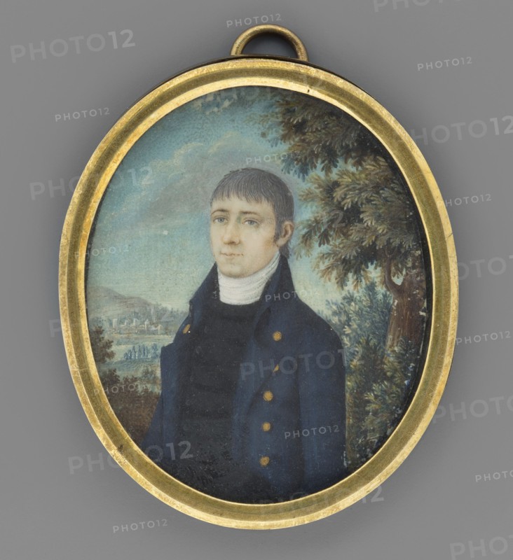 Portrait of a man, unknown painter, Krzeszowice Lesser Poland Voivodeship, plants, trees, man, three-quarter portrait, sky, male portrait, miniature, 1803, height 6.1 cm, width 4.9 cm, An oval pendant with a gold-colored metal frame contains a painted portrait of a young man shown from the chest up, wearing a dark blue coat with gold-colored buttons and a high white collar; he has short brown hair and a pale complexion with a neutral expression. The background shows a light blue sky with soft clouds, a leafy green tree to the right, and a distant landscape with muted green and brown tones. The frame and loop at the top are gold-colored, and the overall image includes shades of blue, green, brown, gold, white, and pale skin tones.