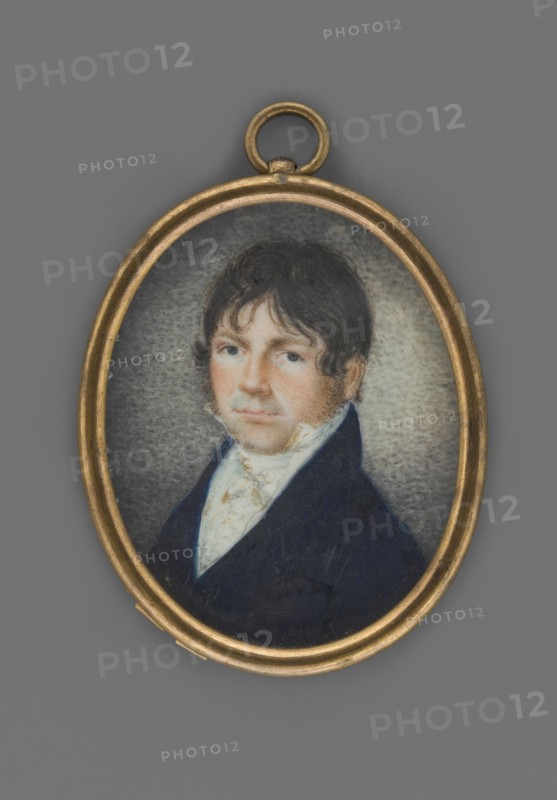 Michal Bulharyn, member of parliament, scribe of the Wolkowysk lands, unknown role classification of the artist, painter author; portrait en three-quarters of a man nobility, male portrait; Polish miniature, 1810, Poland Lithuania?. Bust facing left. Dark hair with a fringe falling over the forehead à la Tytus, dark blue eyes. Shirt collar, cravat, and waistcoat white, navy blue frock coat. Background brownish-gray, stippled, brightened on the right. Binding with gilded brass rim, half-round. On the reverse of the binding inscription: “Mich. Bulharyn / 1785 + 1842.” Miniature, height 5.1 cm, width 4.1 cm., An oval pendant with a gold-toned frame contains a small painted portrait of a man with dark brown hair and sideburns wearing a dark blue coat and a light-colored cravat; the background around the figure is a mottled gray, and the overall visible colors include gold, dark blue, brown, light beige, and gray.