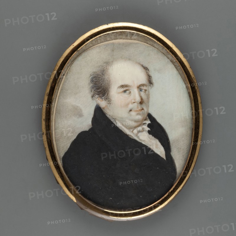 Jedrzej Sniadecki 1768–1838, famous professor of chemistry and medicine, portrait, unknown artist. Half-length three-quarter figure facing right. Dark, graying hair, blue eyes. White shirt collar, cravat and waistcoat, black coat. Background sandy-bluish with gray clouds. Oval brass frame smooth half-cylinder with convex glass. 1815. Miniature; height 6.7 cm, width 5.5 cm., An oval portrait miniature set in a thin gold frame shows a seated man with pale skin and thinning hair that is gray and brown, wearing a dark black coat over a light cream-colored shirt with ruffled collar; his face has blue eyes and a neutral expression, and the background is a soft, muted blend of gray and off-white tones.