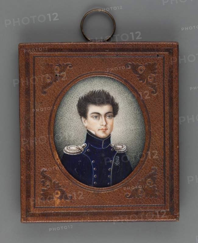 Captain of the Riflemen Józef Maciej Wentzl? 1796–1857, unknown author, en face portrait of a man in a navy blue uniform with yellowish insets, silver buttons and epaulettes, wearing the Virtuti Militari cross. Bust slightly right; black hair, light blue eyes; white shirt collar and black cravat. Style: Polish miniature; amateur painter. Background ash gray, lightened on the right and around the head. Binding: rectangular frame with an oval cut-out of brown leather, two embossed borders at the edges, ornaments in the corners. On the reverse of the binding: inscriptions reading Józef Wentz'l with crossings-out, 1816? and Laniewski. Dimensions: height 4.2 cm, width 3.5 cm., A small rectangular frame with a brown textured surface and embossed decorative corners surrounds an oval portrait; inside the oval is a portrait of a young person with dark brown hair styled upward, pale skin, light blue eyes, and a neutral expression, wearing a dark blue military-style coat with high collar and silv...