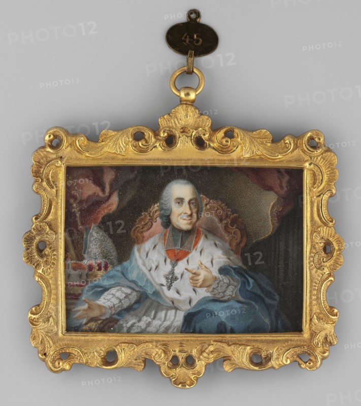 Bishop Joseph Ignaz Philipp von Hessen-Darmstadt 1699–1768, son of Ernest Ludwig and Maria-Theresa de Croy; painted by Nilson, Johann Esaias 1721–1788. Oil miniature 1790, Germany, height 5.0 cm, width 7.1 cm. Seated in an armchair, almost straight ahead, hair gray, wearing a blue cloak with ermine over a white surplice richly decorated with lace, a gold bishop's cross on the chest; knee-length portrait showing bishop's vestments mantelletta, cope, rationale, powdered wig; background shows a fragment of an interior with a curtain. Binding richly decorated with stylized plant motifs mainly acanthus, gilt bronze., A small rectangular painted portrait set in an ornate carved frame with a hanging loop at the top shows a seated man wearing a powdered wig and richly decorated robes; he has a pale face with a faint smile and is gesturing with one hand while the other rests on his lap, and he wears a jeweled cross and a sash. The background includes draped fabric in dark red and brown tones an...