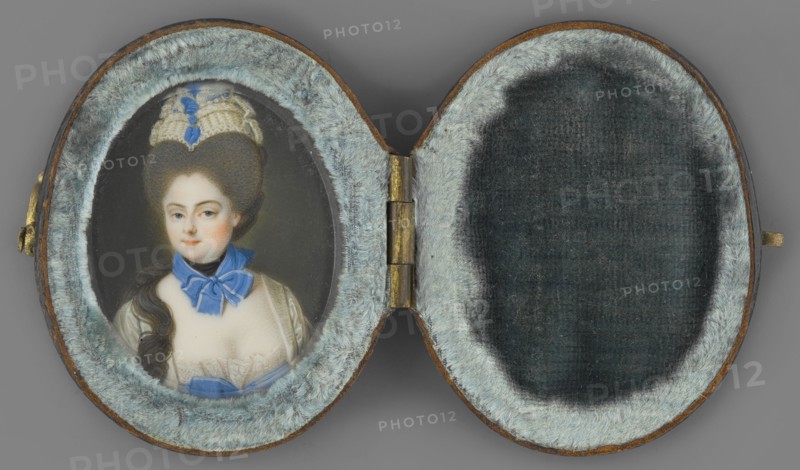 Portrait of a woman in a gray wig. Unknown artist. Aristocratic female three-quarter portrait, bust slightly right, head turned left. Tall gray wig with a white headdress at the top; a long wavy strand of hair falls over the right shoulder. At the neck a black scarf with a light sapphire ribbon tied in a bow. White satin low-cut dress with lace at the bodice and a large light sapphire bow below. Dark gray background. Oval case of dark brown leather, lined with blue velvet inside, closed with a hook. Ca. 1770. Miniature, height 5.6 cm, width 2.9 cm., An open oval case with a hinged center shows a small painted portrait on the left side and a padded interior on the right; the case interior is lined with pale bluish-gray plush fur around each oval opening and darker gray fabric in the central recessed areas, while the exterior edges show brown leather and a small brass hinge and clasp. The painted portrait depicts a person with pale skin, dark brown hair styled high and long with a cream ...