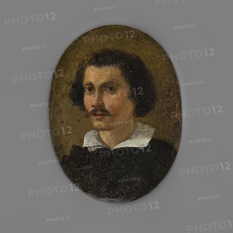 Portrait of a young man, bust three-quarters left. Lush black hair covering the ears, small mustache; turn-down white collar at the neck, black caftan. Olive background. Late amateur copy, miniature, height 7.3 cm, width 5.4 cm, dated 1850–1900. Inscription/attribution note: A. Chamiec 1959., An oval portrait of a man with dark curly hair and a thin mustache, shown from the shoulders up against an olive-brown background; he wears a dark garment with a white collar, and his skin shows warm peach and pink tones with subtle shadowing, while the overall palette includes shades of brown, black, white, olive, peach, and pink.