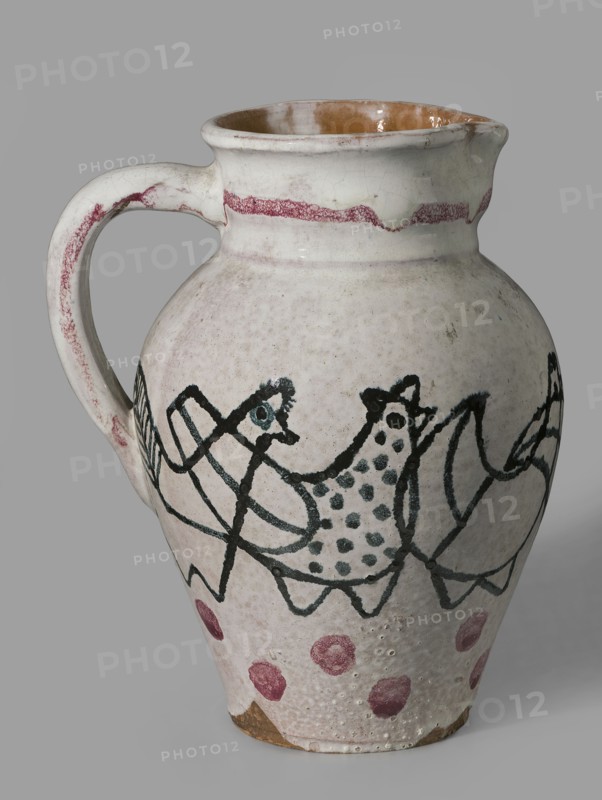 Jug with a handle with zoomorphic decoration: procession of hens; made 1949 by Antoni Kenar 1906–1959, sculptor; co-creators: Office of Production Aesthetics Supervision Warsaw; 1947–1949 and State Secondary School of Fine Arts in Zakopane Zakopane; est. 1876; materials: ceramics; features: zoomorphic representations, linear patterns, painted decorations; unique item; vessel; place of origin: Zakopane; dimensions: height 18.5 cm, width 13.8 cm, depth 16.0 cm., A ceramic pitcher with a rounded body, a curved handle, and a spout, shown against a plain gray background; the exterior glaze is primarily off-white or cream with visible crackling and a glossy brown interior around the rim; decorative painted motifs wrap around the body in dark green or black lines forming abstract bird-like shapes and dotted patterns, with a band of reddish-pink near the neck and several reddish-pink circular spots near the base; areas of wear and small surface pits reveal a tan or light brown clay beneath.