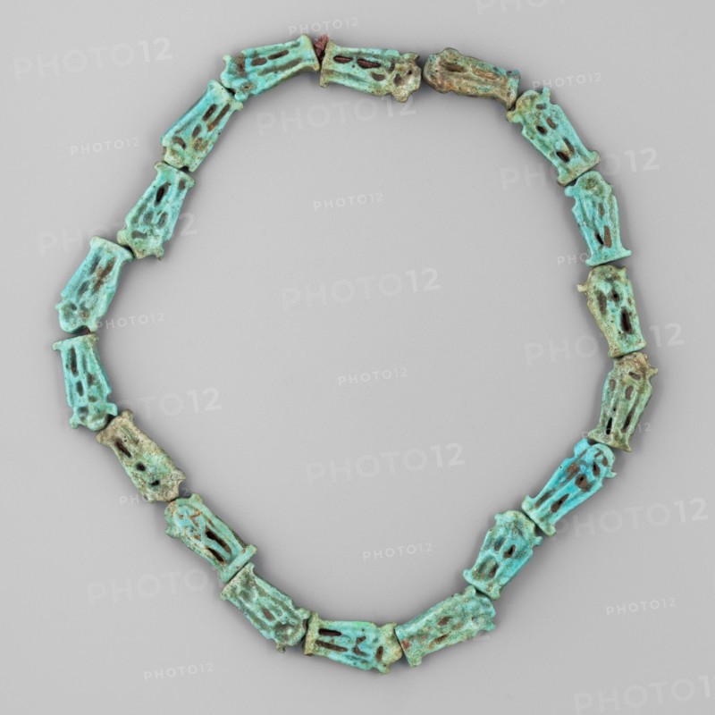 Necklace of 18 amulets, Goluchów Greater Poland Voivodeship, ankhs, Scen.Gal.Eg., necklaces, uas iconographic, ca. 1550–1295 BC; New Kingdom, 18th Dynasty, Egypt, amulet, jewelry, height 27 cm, A necklace composed of a continuous loop of similar carved beads arranged in an oval shape on a neutral gray background, the beads are elongated and slightly irregular with openwork sections and rough surfaces, showing a range of turquoise and green tones with areas of darker brownish and bluish discoloration and some subtle variations in patina across the pieces.
