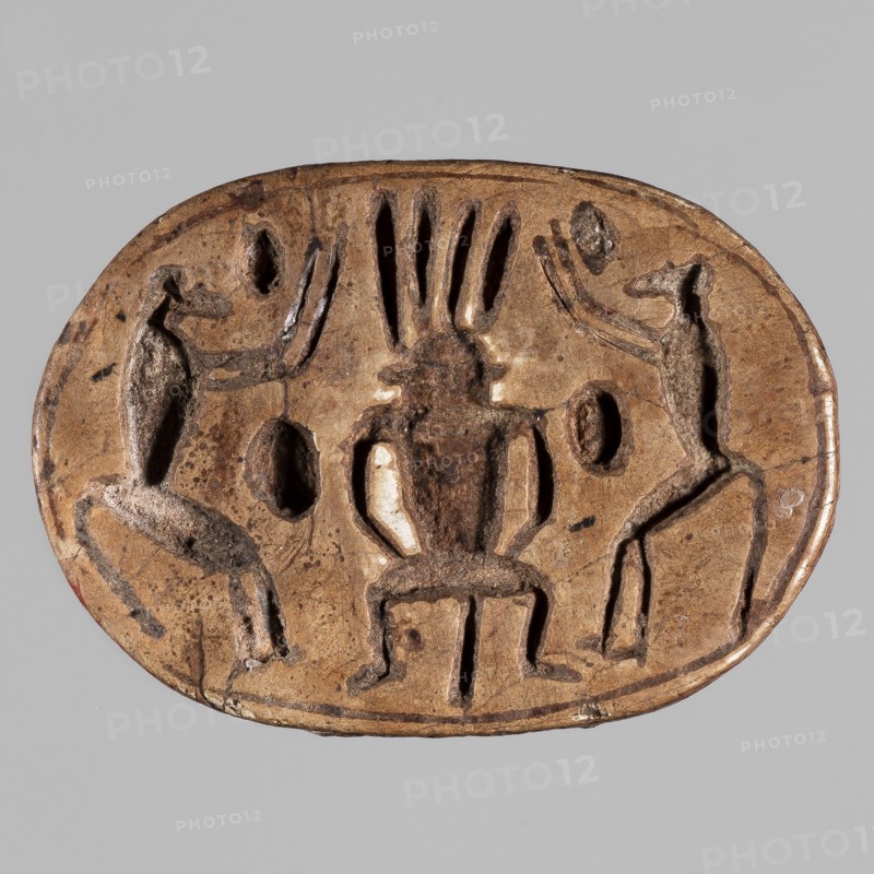 Scarab with a depiction of two baboons adoring Bes; on the reverse, a convex image of a scarab occupies the center of the oval surface, decorated with engraved parallel lines. ca. 1295–1186 BC; New Kingdom, 19th–20th Dynasty, Egypt. Scarab amulet; height 2.5 cm, width 3.6 cm., An oval, carved object in brown and tan tones sits against a light gray background; the surface shows a darker brown central figure seated on a low stool with elongated vertical elements rising above its head, flanked by two upright humanlike figures on either side that face inward with raised arms; the left and right figures and the central figure are carved in relief with visible grooves and rounded depressions around them, and the object's edges show slight wear and darker speckling.