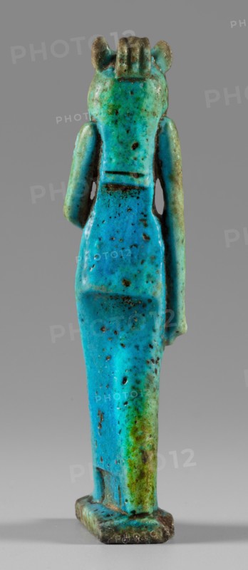 Amulet - figurine of a lion-headed goddess. A lion-headed goddess, in a tripartite wig and a narrow robe, walks with a lotus scepter in her left hand the right one lowered. Presumably the goddess Sekhmet; may relate to Wadjit or Bastet. Grave good; Egyptian, Late Period, 664–332 BC. Material: amulet; height 8.8 cm, width 1.7 cm., A vertical turquoise and green small statuette of a standing human-like figure shown from the back against a gray background, with a smooth elongated body and visible arm shapes at the sides, a rectangular base at the feet, a rounded head with short ridged detail at the top and small ear-like protrusions, a speckled and pitted surface with darker brown spots and areas of weathering, and visible transitions between bright blue-green, teal, and patches of olive green and brown.